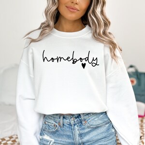 May include: White sweatshirt with the text "homebody" in black script with a small black heart.