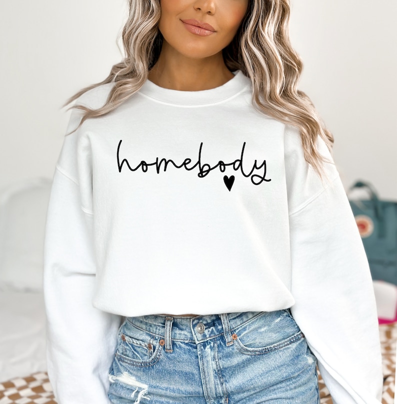 May include: White sweatshirt with the text "homebody" in black script with a small black heart.