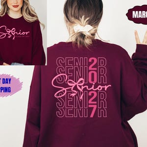 May include: Maroon sweatshirt with the word "Senior" in a cursive font, with "Class of 2023" below it. The back of the sweatshirt has the word "Senior" repeated vertically with a bow graphic. The sweatshirt is a dark red color.
