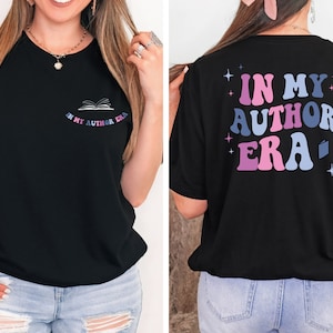 Puede incluir: Camiseta negra con un gr&aacute;fico en la parte delantera que dice "In My Author Era" con un icono de libro. La parte posterior de la camiseta tiene un gr&aacute;fico m&aacute;s grande que dice "In My Author Era" en una fuente retro con estrellas y un icono de libro.