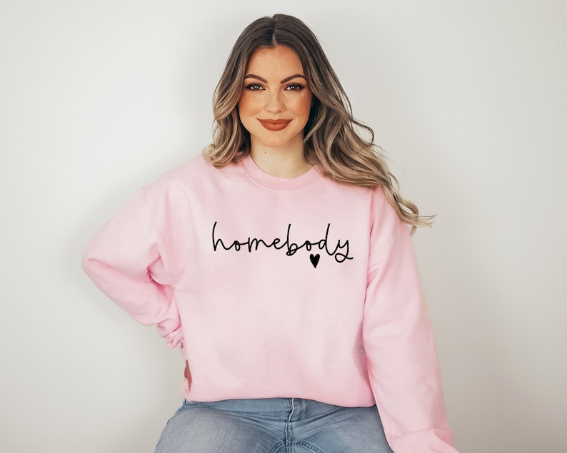 May include: A pink sweatshirt with the text "homebody" in black script with a small black heart.