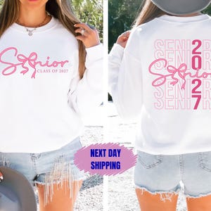 May include: White sweatshirt with the word "Senior" in pink script and a bow design. The text "Class of 2027" is below the word "Senior". The back of the sweatshirt has the word "Senior" repeated vertically with the numbers "2027".