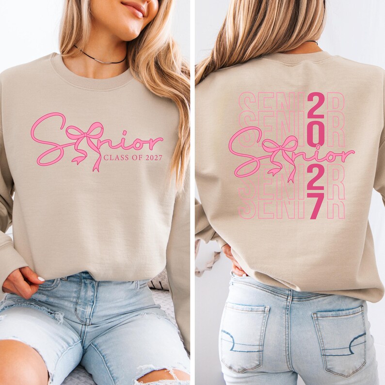 May include: Beige sweatshirt with pink "Senior" script and bow design. The front features "Senior Class of 2027" in pink. The back has a stacked pink "Senior 2027" design. The sweatshirt is a casual garment.