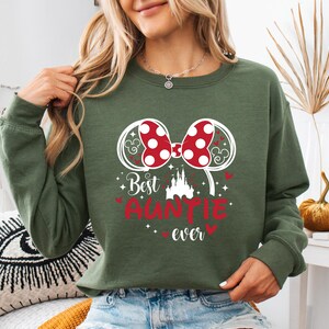 May include: Green sweatshirt with a red and white polka dot bow design and the words "Best Auntie Ever". The design includes a castle and heart accents. The sweatshirt is a long-sleeved crew neck.