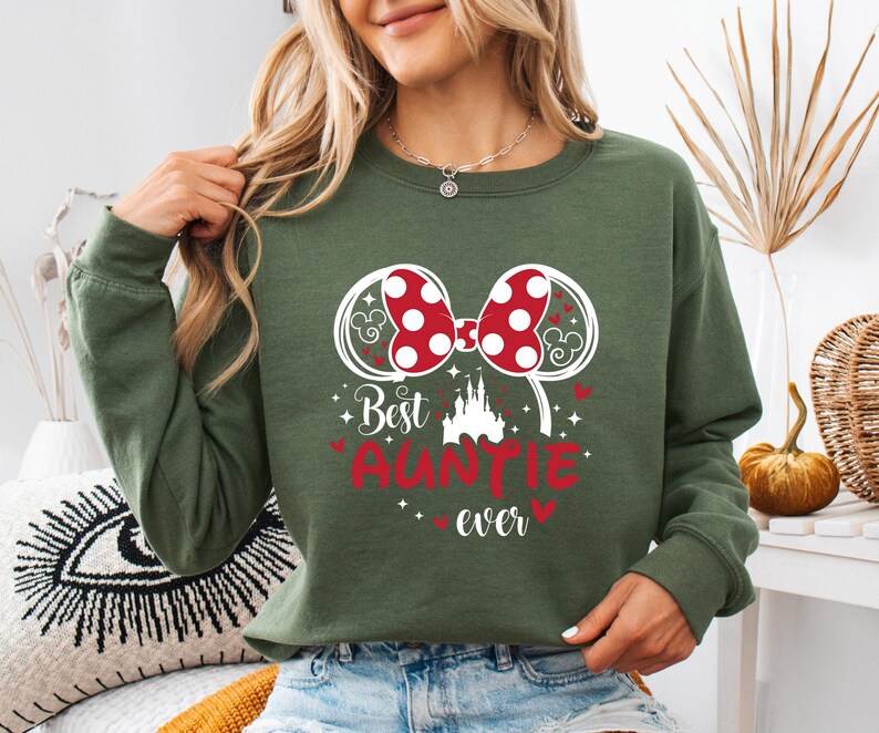 May include: Green sweatshirt with a red and white polka dot bow design and the words "Best Auntie Ever". The design includes a castle and heart accents. The sweatshirt is a long-sleeved crew neck.