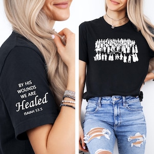 May include: Black t-shirt with white text on the sleeve that reads "By His Wounds We Are Healed" and "Isaiah 53:5". The other black t-shirt has a white graphic of people and animals. Both shirts are short-sleeved.