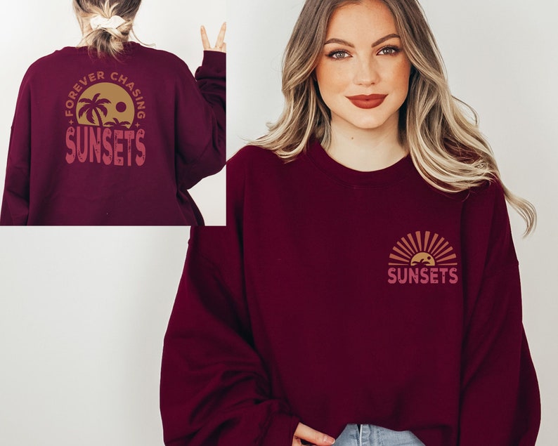 May include: A maroon sweatshirt with a graphic on the front and back. The front graphic is a stylized sunset with palm trees and the word "SUNSETS". The back graphic is a circle with the words "FOREVER CHASING SUNSETS" and a palm tree.