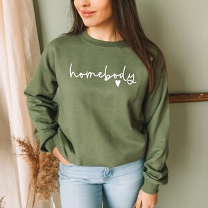 May include: A green sweatshirt with the text "homebody" in white lettering and a small white heart.