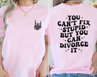 May include: Pink t-shirt with a black skeleton hand making a rock and roll sign on the front and the text "YOU CAN'T FIX +STUPID+ BUT YOU +CAN+ DIVORCE IT" on the back.