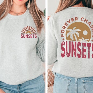 May include: Gray sweatshirt with a red "SUNSETS" graphic on the front and a red "FOREVER CHASING SUNSETS" graphic on the back. The graphic on the back features a palm tree and a sun.