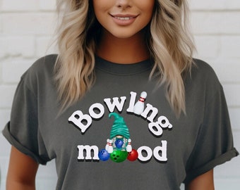 May include: A grey t-shirt featuring a graphic of a gnome holding bowling pins and bowling balls. The text "Bowling mood" is printed on the shirt.