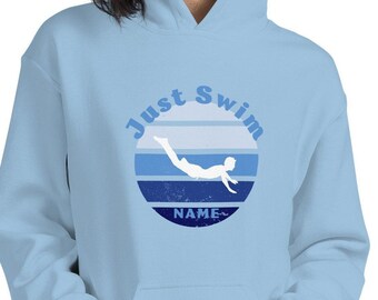 Op de afbeelding: Een lichtblauwe hoodie met een afbeelding van een persoon die zwemt in een cirkel met de tekst "Just Swim" en "NAME" onder de afbeelding.