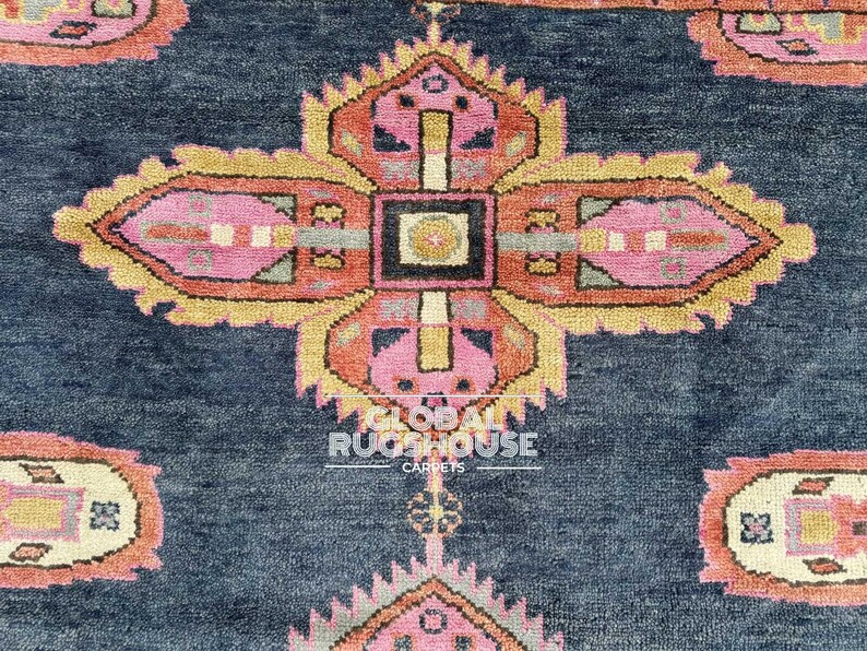 Op de afbeelding: Close-up van een marineblauw tapijt met een herhalend patroon van gestileerde bloemen en geometrische vormen in roze, oranje en geel. Het tapijt heeft een textuur en een centraal medaillonontwerp.