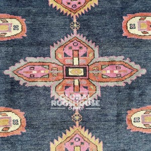 Op de afbeelding: Close-up van een donkerblauw tapijt met een herhalend patroon van roze, oranje en gele bloemachtige ontwerpen. Het tapijt heeft een getextureerd uiterlijk en de woorden "GLOBAL RUGSHOUSE CARPETS" zijn zichtbaar.