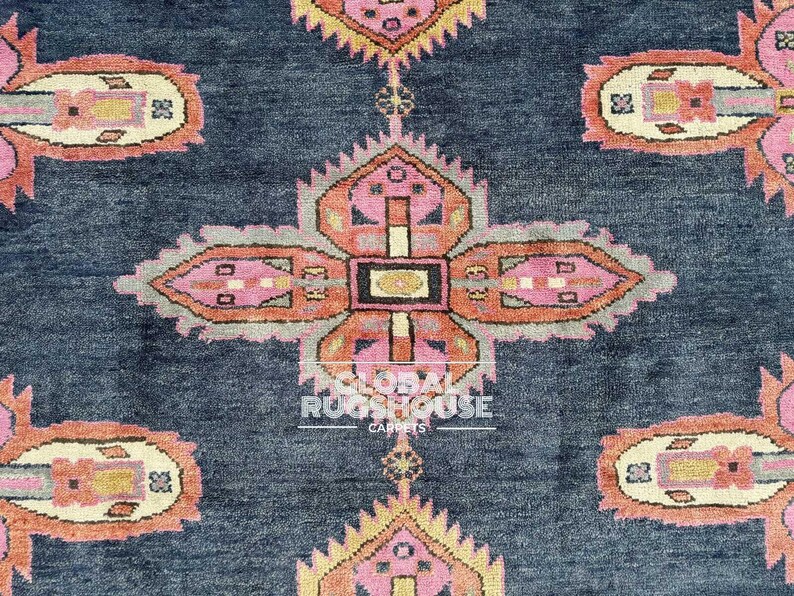 Op de afbeelding: Close-up van een donkerblauw tapijt met een herhalend patroon van roze, oranje en gele bloemachtige ontwerpen. Het tapijt heeft een getextureerd uiterlijk en de woorden "GLOBAL RUGSHOUSE CARPETS" zijn zichtbaar.
