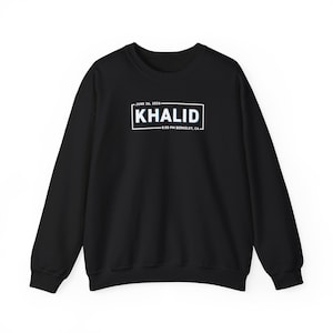 May include: A black crewneck sweatshirt featuring a white rectangular graphic on the chest. The text inside reads KHALID, JUNE 26, 2026, and 8:00 PM BERKELEY, CA. The design includes long sleeves, a ribbed neckline, and ribbed cuffs at the wrists and waist.