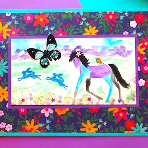 May include: A colorful greeting card with a floral patterned border. The card features a watercolor painting of a purple horse with a bird, blue rabbits, and a butterfly. The background is a field with purple clouds.