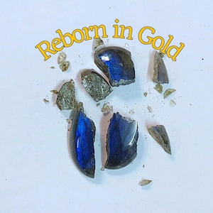 Könnte beinhalten: Zerbrochene Teile eines Edelsteins mit schillernden blauen und grünen Farbtönen, verstreut auf einer weißen Oberfläche. Der Text "Reborn in Gold" ist in gelber Schrift über dem Bild geschrieben.