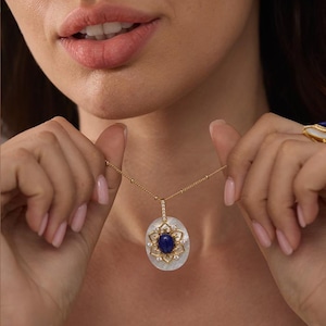 May include: A gold chain necklace with a pendant featuring a blue gemstone surrounded by smaller white gemstones set in a white mother-of-pearl oval.