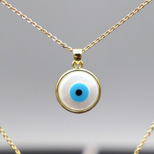 May include: A gold chain necklace with a white and blue evil eye pendant. The pendant is round and has a blue eye with a black pupil.