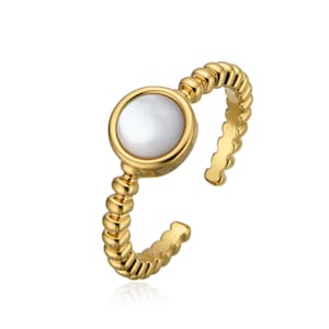 Puede incluir: Un anillo ajustable de color dorado con una piedra central redonda de nácar blanco. La banda presenta un diseño texturizado y con cuentas. El anillo está abierto en la parte inferior, lo que permite el ajuste de tamaño. Joyería.