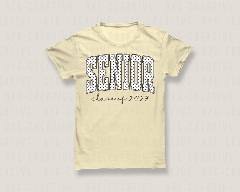 Puede incluir: Camiseta amarilla clara con la palabra "SENIOR" en letras grandes blancas con lunares. Debajo, el texto "class of 2027" est&aacute; escrito en negro fino. La camiseta tiene mangas cortas y cuello redondo.
