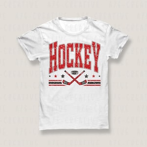 K&ouml;nnte beinhalten: Wei&szlig;es T-Shirt mit einem rot-schwarzen Hockey-Design. Das Wort "HOCKEY" ist in einer Schriftart im College-Stil dargestellt. Darunter befinden sich gekreuzte Hockeyschl&auml;ger, ein Puck und Sterne.