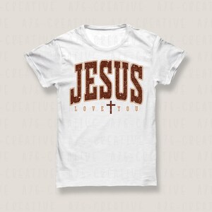 Pode incluir: Camiseta branca com um gr&aacute;fico marrom desbotado que diz "JESUS LOVE YOU" com uma pequena cruz entre as palavras "LOVE" e "YOU".