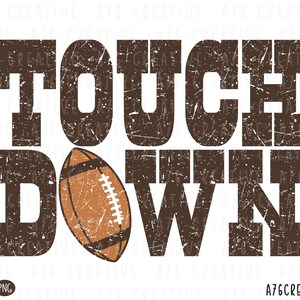 May include: A distressed brown graphic with the words "TOUCH DOWN" and a football illustration. The text is in a bold, blocky font with a textured, worn appearance. The football is brown with white laces.