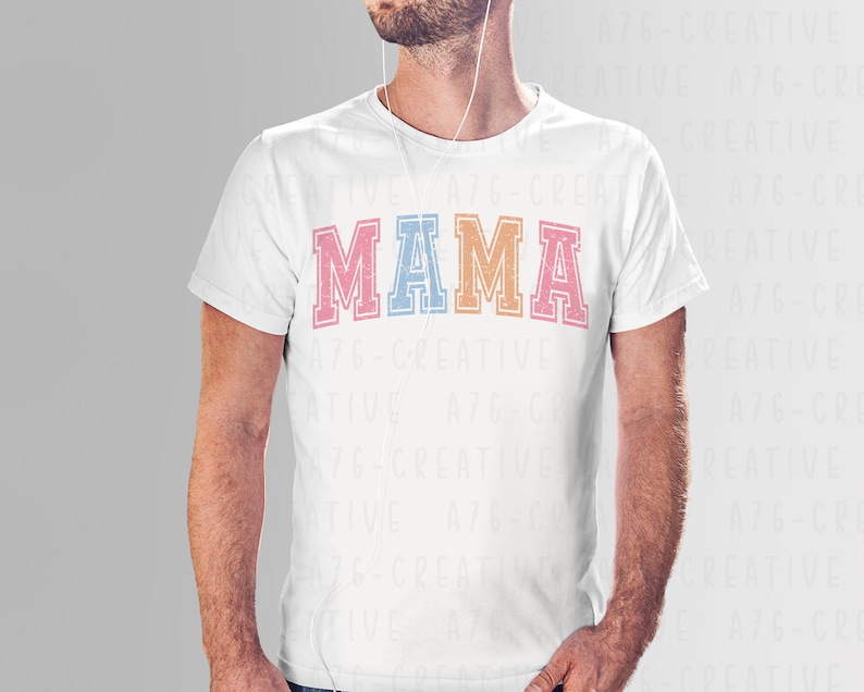 May include: A white t-shirt with the word "MAMA" printed in colorful block letters. The letters are outlined in black and have a vintage, distressed look.