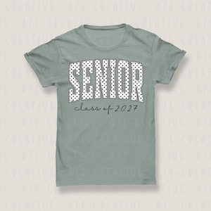 Puede incluir: Camiseta verde salvia con la palabra "SENIOR" en blanco, con lunares. Debajo, el texto "class of 2027" est&aacute; escrito en una fuente manuscrita. La camiseta es de cuello redondo.