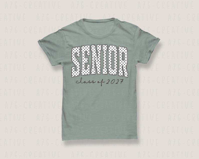 Puede incluir: Camiseta verde salvia con la palabra "SENIOR" en blanco, con lunares. Debajo, el texto "class of 2027" est&aacute; escrito en una fuente manuscrita. La camiseta es de cuello redondo.