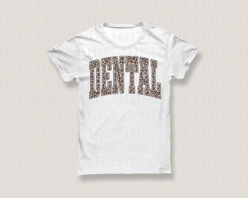 May include: A white t-shirt with the word "DENTAL" printed across the front in a bold, arched font. The letters are filled with a brown and tan leopard print pattern, creating a striking contrast against the white fabric.
