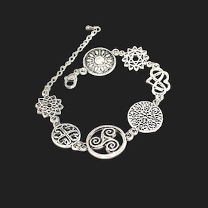 Könnte beinhalten: Silberfarbenes Armband mit verschiedenen dekorativen Anhängern. Die Anhänger umfassen einen Sonnenstrahl, eine Blume, einen keltischen Knoten und ein Spiraldesign. Das Armband hat eine Kettenverlängerung und einen Karabinerverschluss. Das Armband ist vor schwarzem Hintergrund.