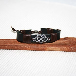 May include: A black leather bracelet with brown leather wrappings and a silver infinity heart charm.