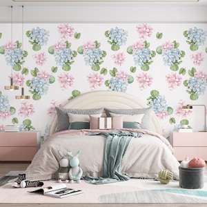 May include: A bedroom with a white wall featuring a floral wallpaper pattern with pink and blue flowers. The bed is made with a white duvet and a light blue throw blanket. There are two bedside tables with lamps on either side of the bed.