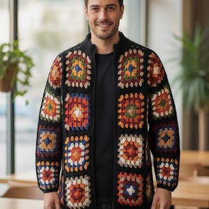 Puede incluir: Un cárdigan negro con cremallera y un colorido patrón de cuadrados de la abuela. Los cuadrados presentan tonos de rojo, naranja, amarillo, azul y verde. El cárdigan se lleva sobre una camisa negra y con pantalones negros.