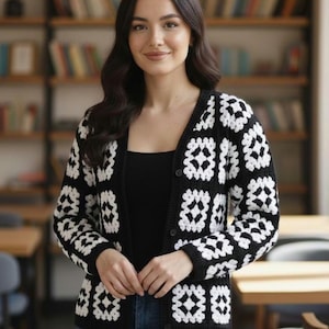 Könnte beinhalten: Eine schwarz-weiße Häkelstrickjacke mit Knopfleiste. Die Strickjacke hat ein sich wiederholendes quadratisches Muster in Weiß auf schwarzem Hintergrund. Die Frau im Bild trägt ein schwarzes Oberteil und blaue Jeans.