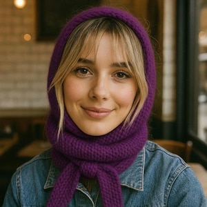Puede incluir: Un conjunto de capucha y bufanda de punto morado. La capucha enmarca la cara y el cuello, con una bufanda que se ata en el pecho. El conjunto está hecho de un tejido de punto grueso y texturizado. La persona lleva una chaqueta vaquera.