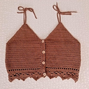 以下が含まれることがあります： ボタン留めとフリルのあるヘムを持つ、茶色のクロシェタンクトップ。ストラップは肩で結ばれています。トップはシンプルなステッチパターンで作られており、ゆったりとしたフィット感です。 @crochet_sevdam