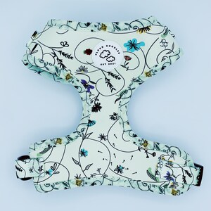 Könnte beinhalten: Ein hellgrünes Hundegeschirr mit einem weißen Blumenmuster und einem runden Logo mit der Aufschrift "Cloud Doodles Est. 2021".