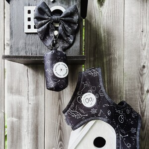 May include: A set of black dog accessories, including a bow, harness, and waste bag dispenser. The items are decorated with a white pattern of bones, spiderwebs, and other spooky designs. The waste bag dispenser has the text "DOODLES CLOUD DOODLES".