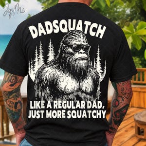 Könnte beinhalten: Schwarzes T-Shirt mit einem weißen Aufdruck eines Bigfoot mit Sonnenbrille und dem Text "DADSQUATCH" über dem Bild. Unter dem Bild steht der Text "LIKE A REGULAR DAD, JUST MORE SQUATCHY."