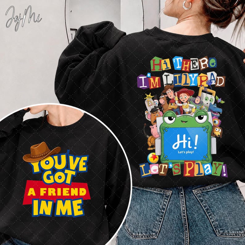 Puede incluir: Una sudadera negra con un gr&aacute;fico de una rana verde que sostiene un cartel azul que dice Hi! Let's play! rodeada de personajes animados y el texto Hi There I'm Lilypad. El frente muestra un sombrero de vaquero marr&oacute;n y You've Got A Friend In Me.