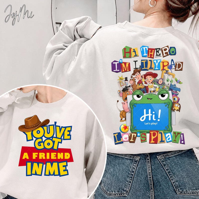 Puede incluir: Una sudadera blanca de manga larga con un gr&aacute;fico de un sombrero de vaquero marr&oacute;n y el texto "YOU'VE GOT A FRIEND IN ME" en el frente, y en la parte posterior varios personajes animados con una rana verde y el texto "HI THERE I'M LILYPAD HI! LET'S PLAY!"