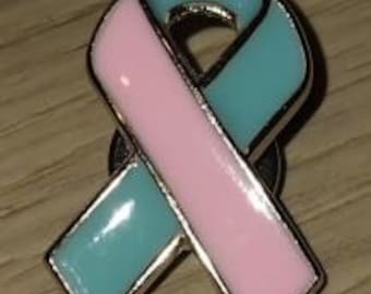 Peut inclure: Une broche en forme de ruban de sensibilisation avec une finition en émail lisse et brillant. Le ruban est divisé en deux sections distinctes, l'une colorée en rose pastel doux et l'autre en bleu sarcelle clair, le tout bordé d'argent.