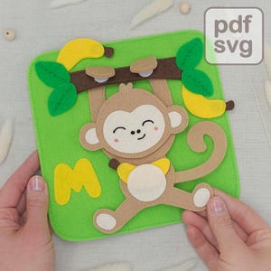 May include: A felt monkey hanging from a brown branch with bananas and green leaves, set against a green background. The monkey has a smiling face and is holding a banana. The letter "M" is also on the green background. The image has the text "pdf svg".