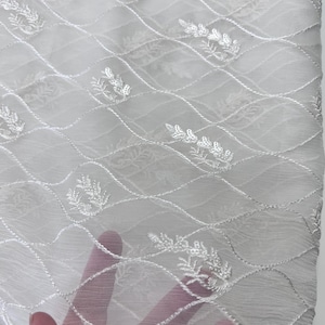 May include: White sheer fabric with a delicate floral embroidery pattern. The fabric has a scalloped edge.