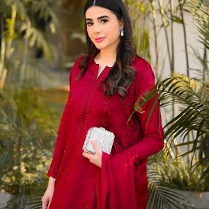 May include: A woman wearing a red embroidered dress with a silver clutch.