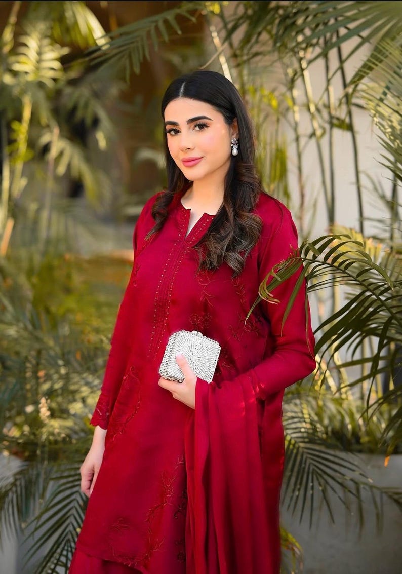 May include: A woman wearing a red embroidered dress with a silver clutch.